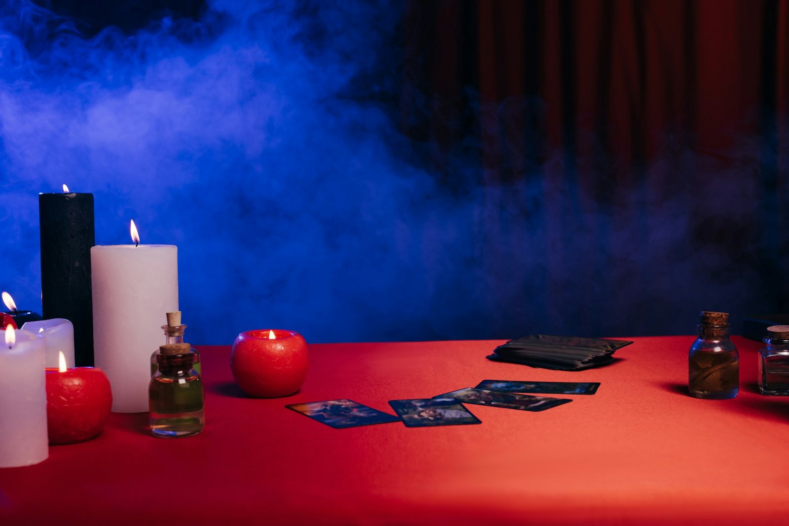 KYIV, UKRAINE - JUNE 29, 2022: burning candles and tarot cards on red table near blue smoke on black